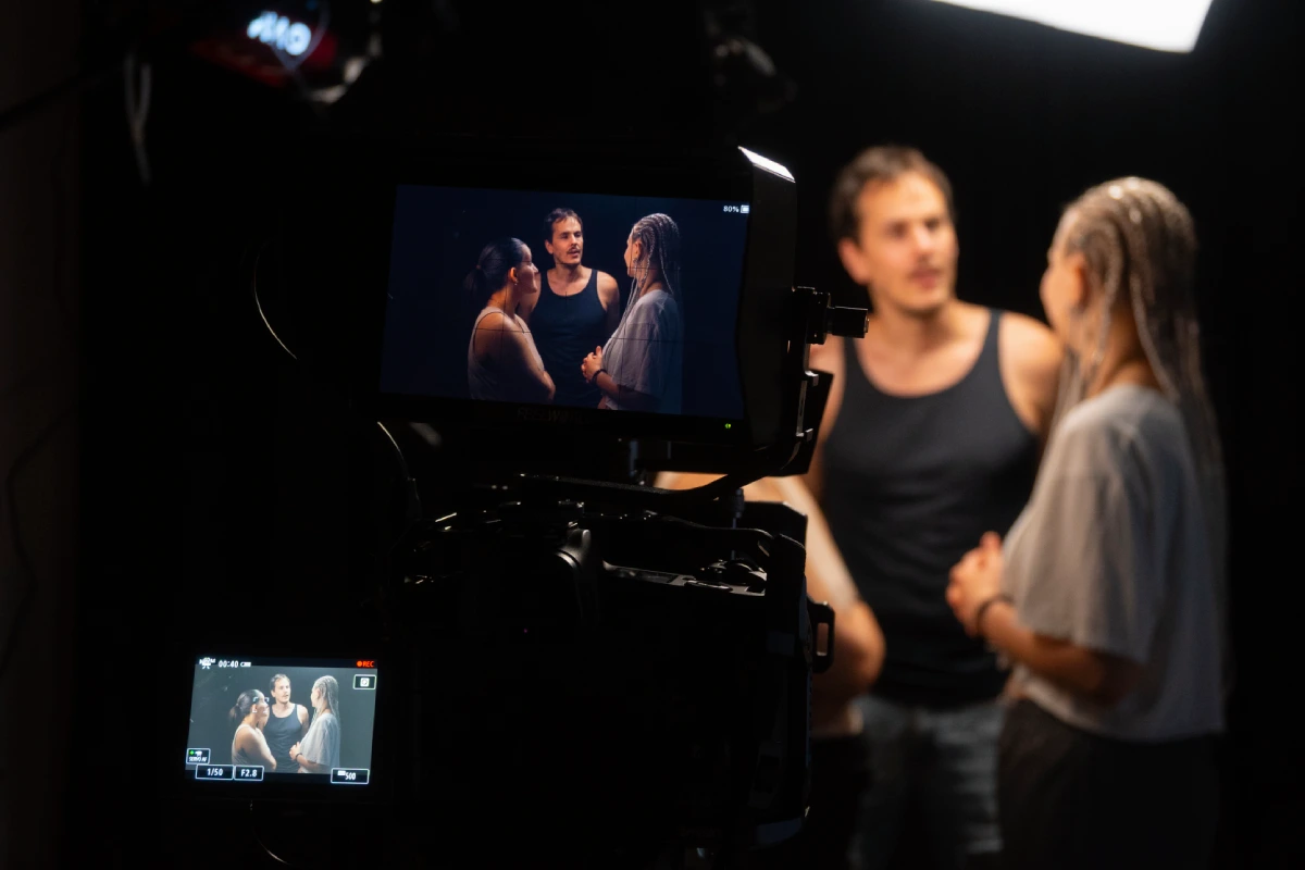 Cámara profesional grabando una escena con tres intérpretes en pleno conflicto dramático, mostrando monitor de referencia y acción real en set.